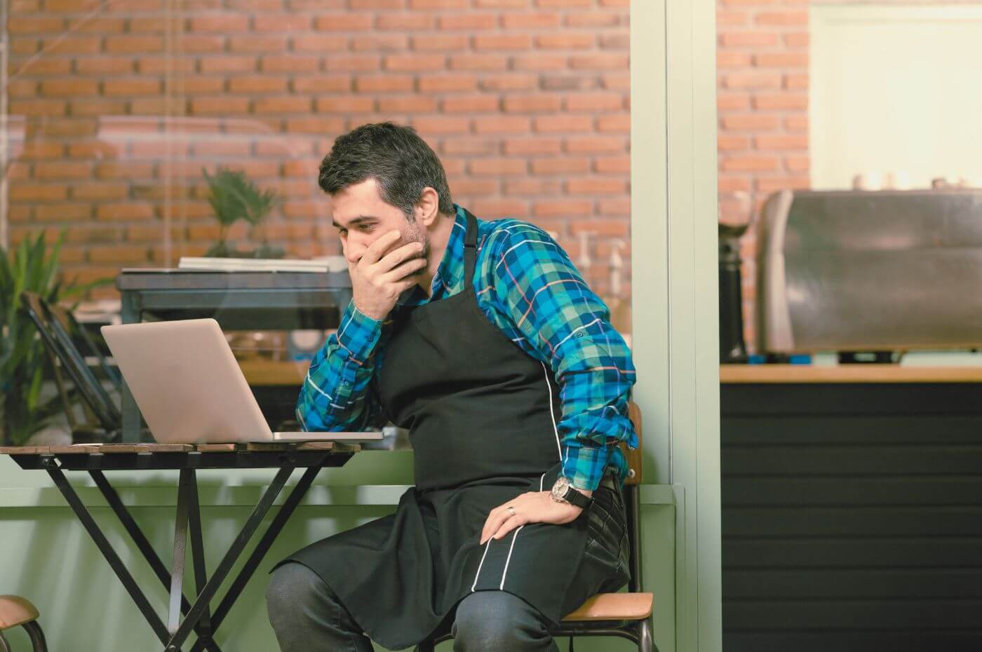 man with an apron looking at a restaurant website on a laptop