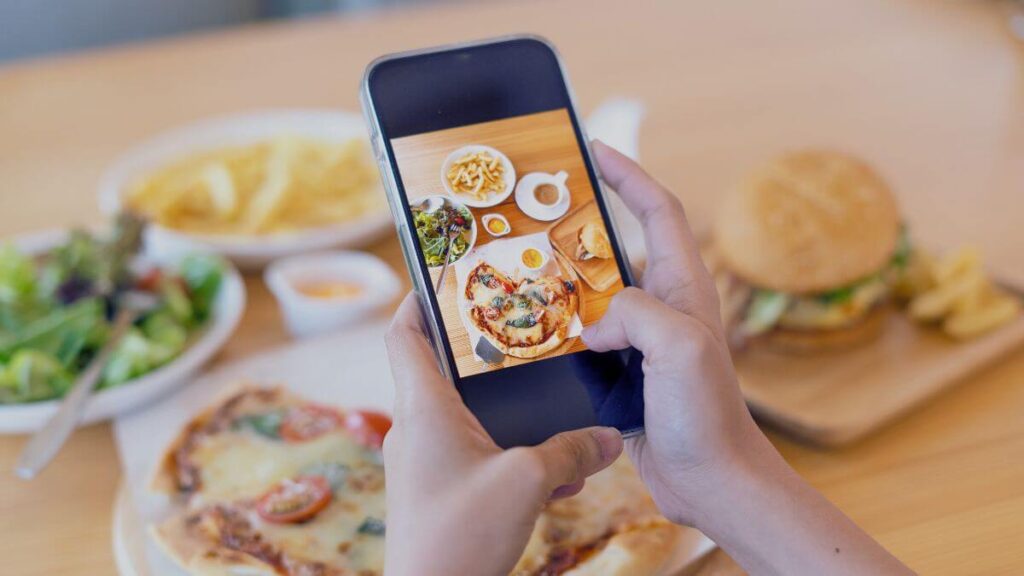 Customer taking a picture of their food and leaving a review on their smartphone at a dining table